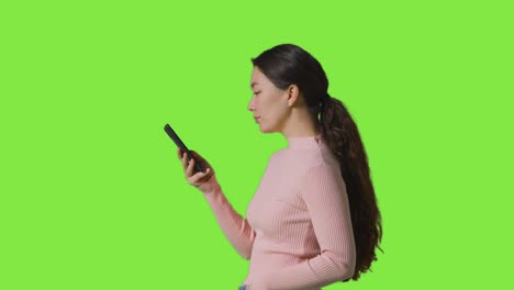 Profilstudioaufnahme-Einer-Frau,-Die-Ihr-Mobiltelefon-Vor-Grünem-Bildschirm-Benutzt